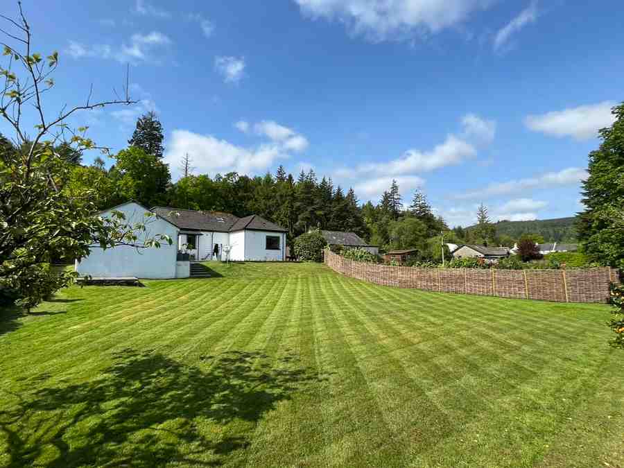 Massive back garden almost that of a mini farm, with a cottage building up ahead, grass perfectly cut in stripes with squares as