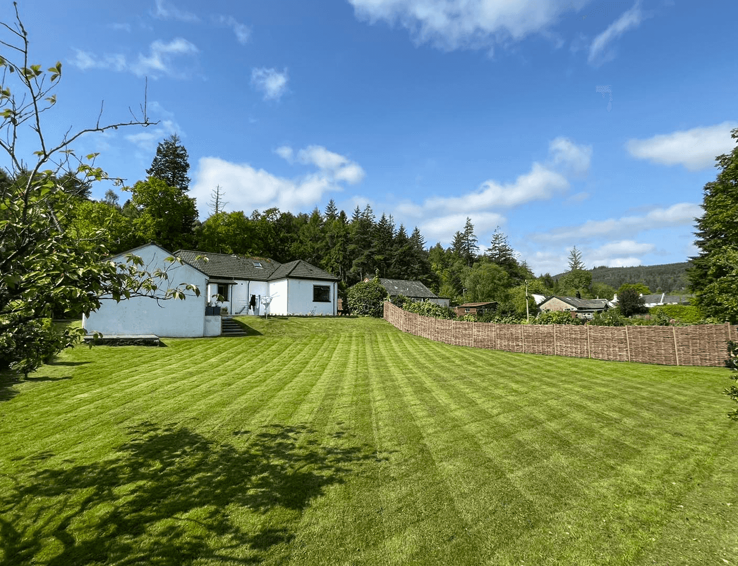 Massive back garden almost that of a mini farm, with a cottage building up ahead, grass perfectly cut in stripes with squares as well